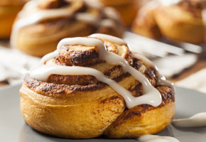 a close up of a homemade cinnamon roll drizzled with icing, on a gray plate