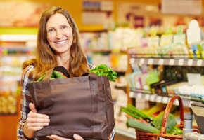 Smiling woman holding full shopping bag with vegetables in organ