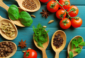 Tomatoes with wooden spoons with fresh herbs and spices on wooden background